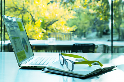 Laptop mit Geschäftszahlen, Notizbuch, Brille - grüne Farbtönung